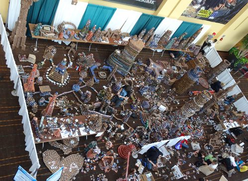 Installazione artistica vista dall'alto, fatta interamente di scatole e bustine di carte Magic, a una fiera